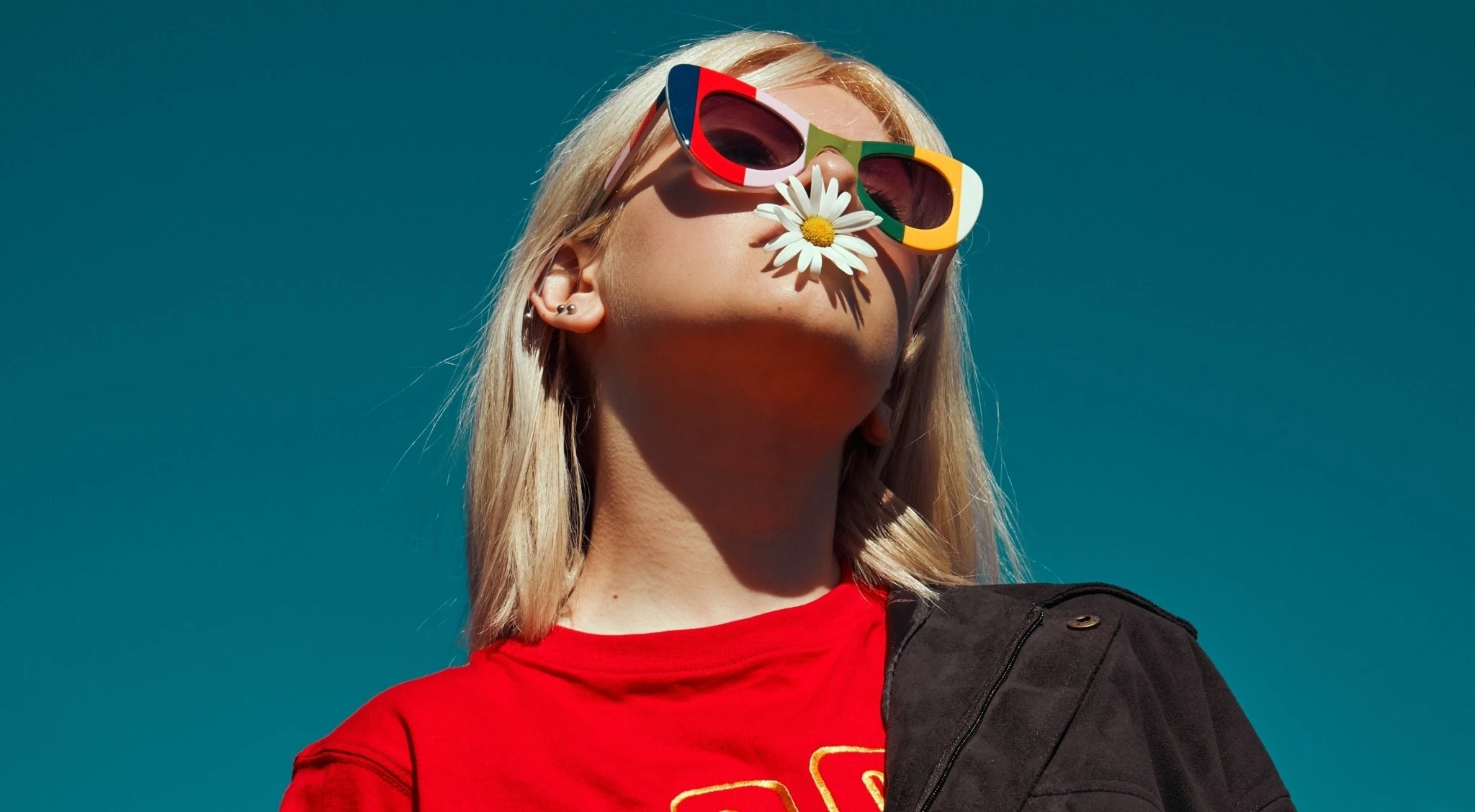 Une fille à la mode portant des lunettes et une fleur dans la bouche