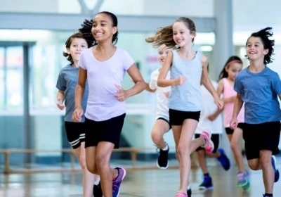 A group of diverse kids run through the gym while laughing. They are racing each other and trying to be the fastest.